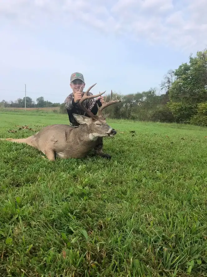 Young hunter proudly displays a large buck with velvet antlers raised.
